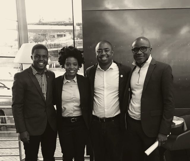 Four people standing together after a working session, photographed in daylight against a glass frontage.